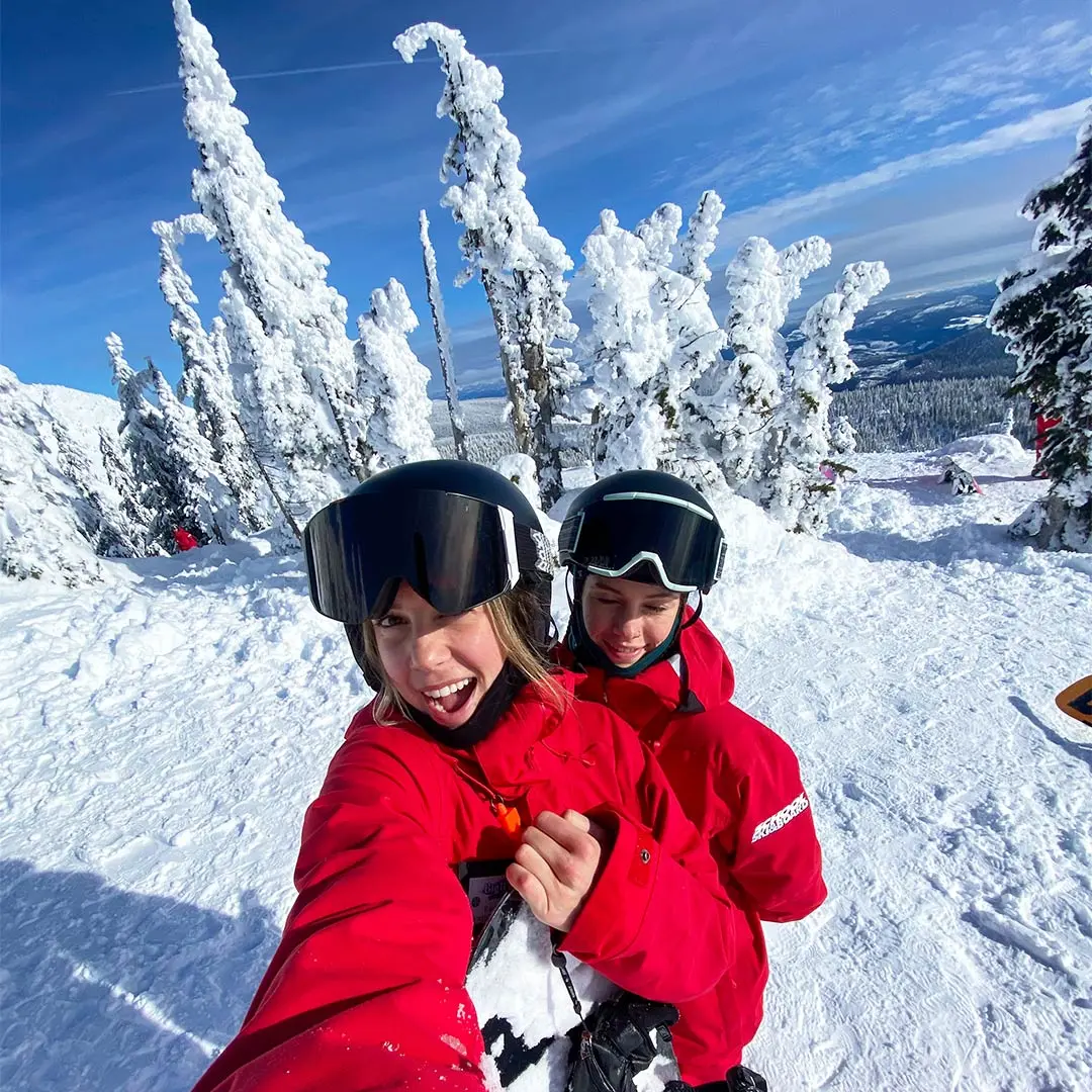 2 girls in red snow gear smile with blue sky in background